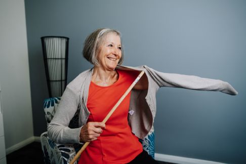 Older lady using a dressing stick to put on a cardigan 