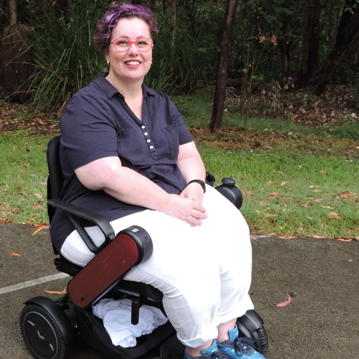 Smiling woman with white cane holding “Assistive Tech RULES!” sign
