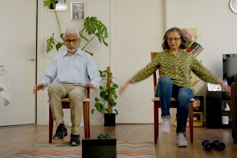 Older couple exercising at home while sitting down