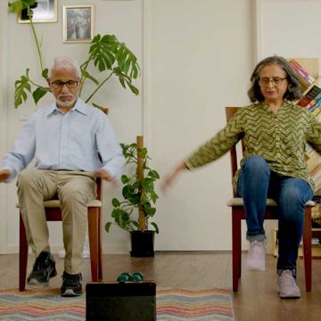 Older couple exercising at home while sitting down