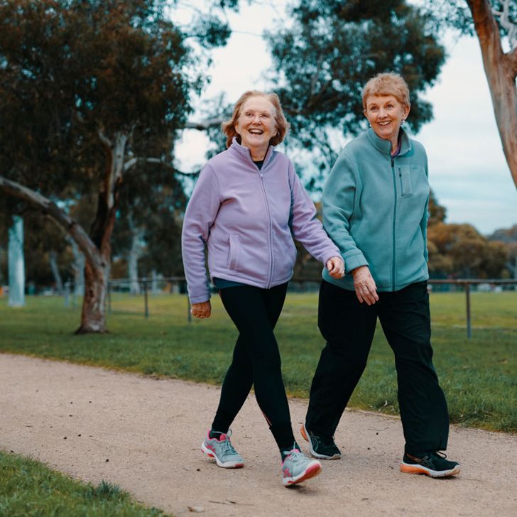 Two women walking in a park area, both are smiling.