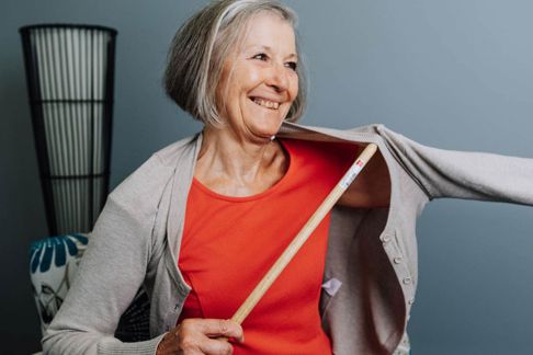 A woman using a dressing aid to help her put on a cardigan  