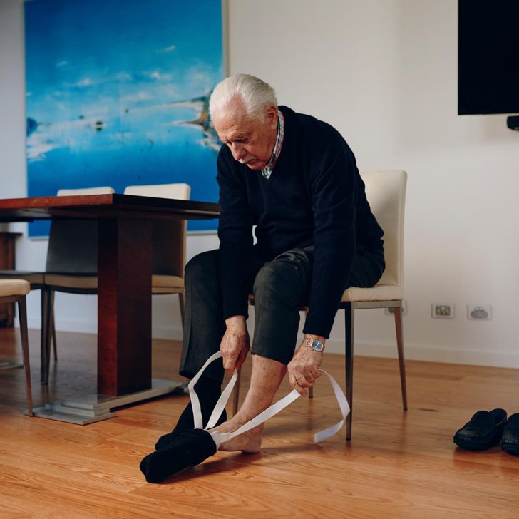 A woman kneeling beside a man sitting as he puts his shoe on using a dressing aid.