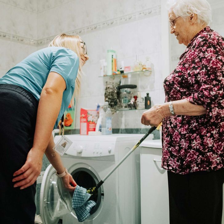 Support worker demonstrating the Grab arm AT with a client in a laundry.