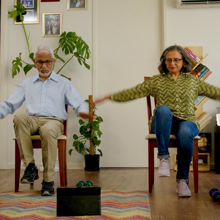 A senior couple doing chair yoga at home