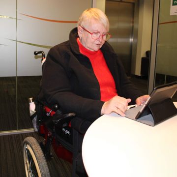 A senior lady sat in her wheelchair looking at her laptop