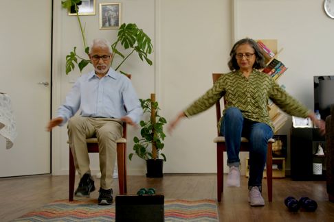 Older couple exercising at home while sitting down