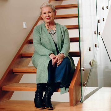 A senior lady sat on her wooden stairs in her home.