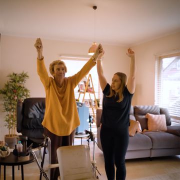 Aged care worker stretching with an older woman in a living room