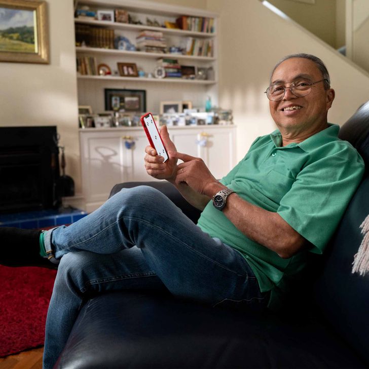 An older man sat on his sofa using his mobile phone