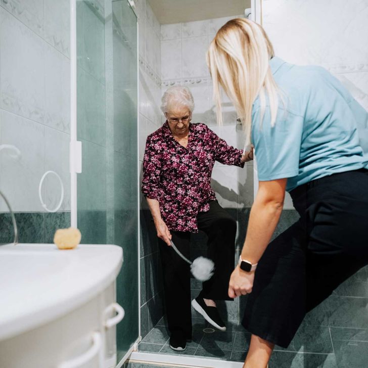 Senior lady being shown a long-handled sponge for shower use