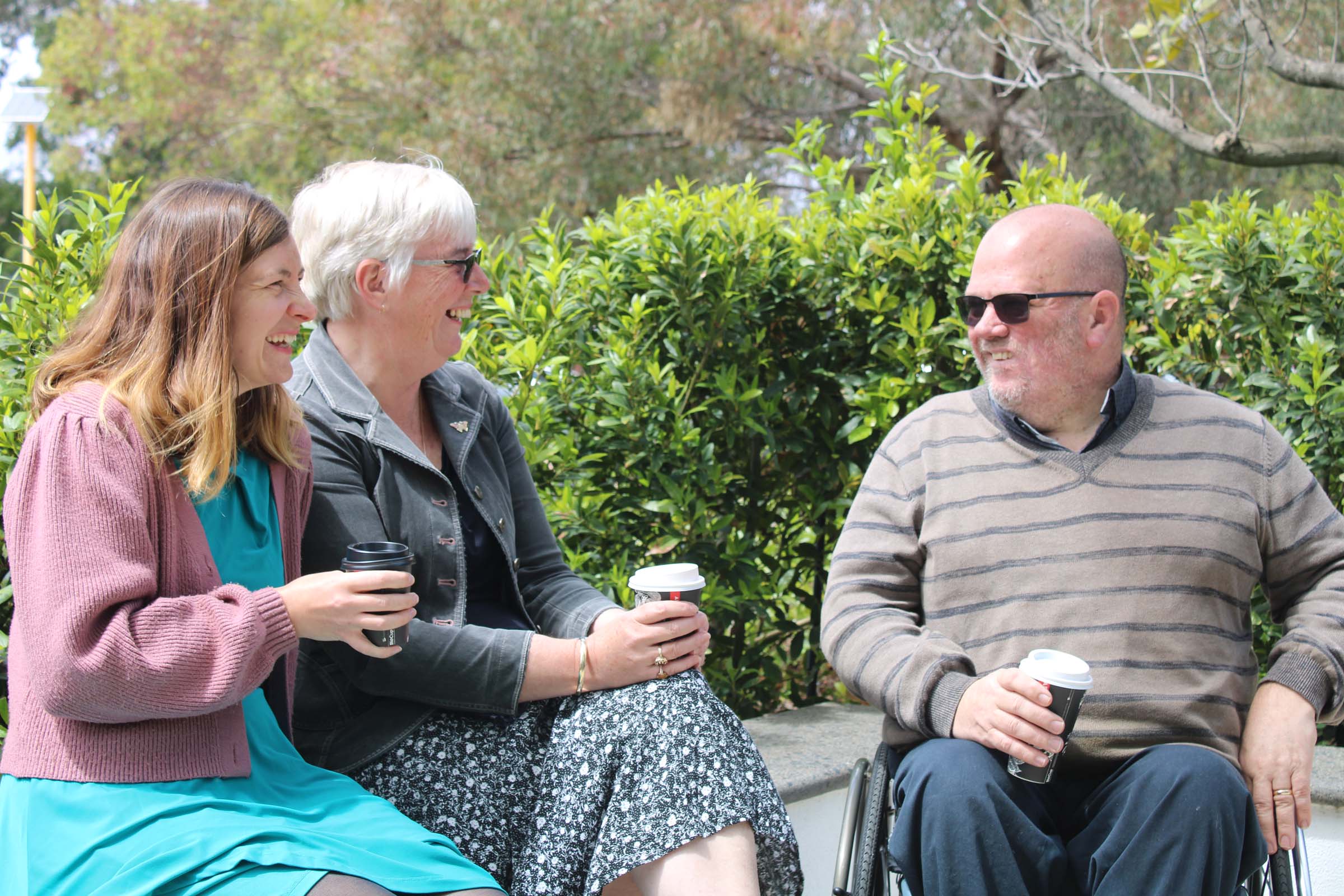 Three people sit down together with coffees. Three people sit down together with coffees.