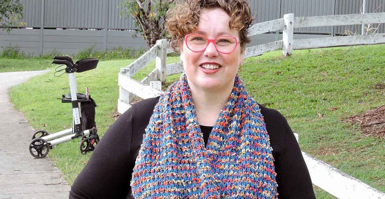 Nerine-walker-and-cane-2-socials A lady wearing glasses, a big smile and a colourful scarf.