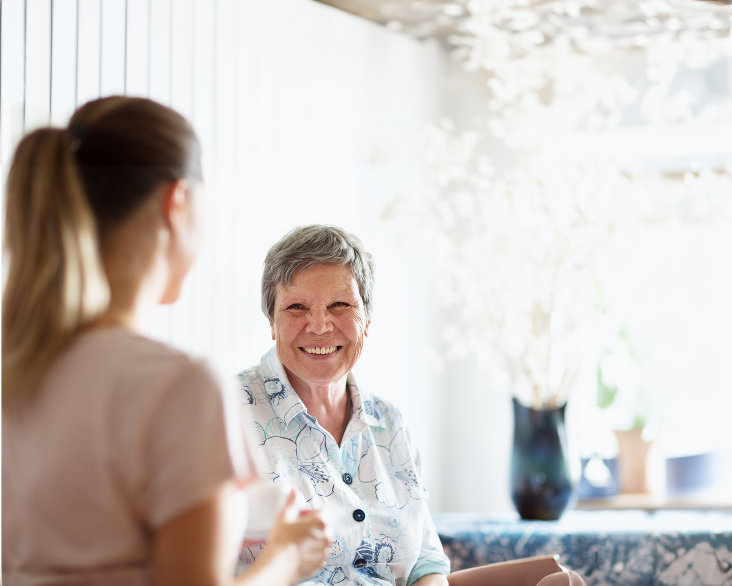 A woman is seated at a table smiling at another woman with her back to the camera.