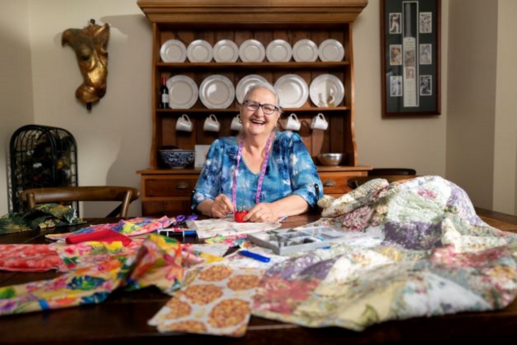 older woman smiles as she sews