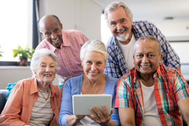 Five older people smile at the camera one holds a tablet