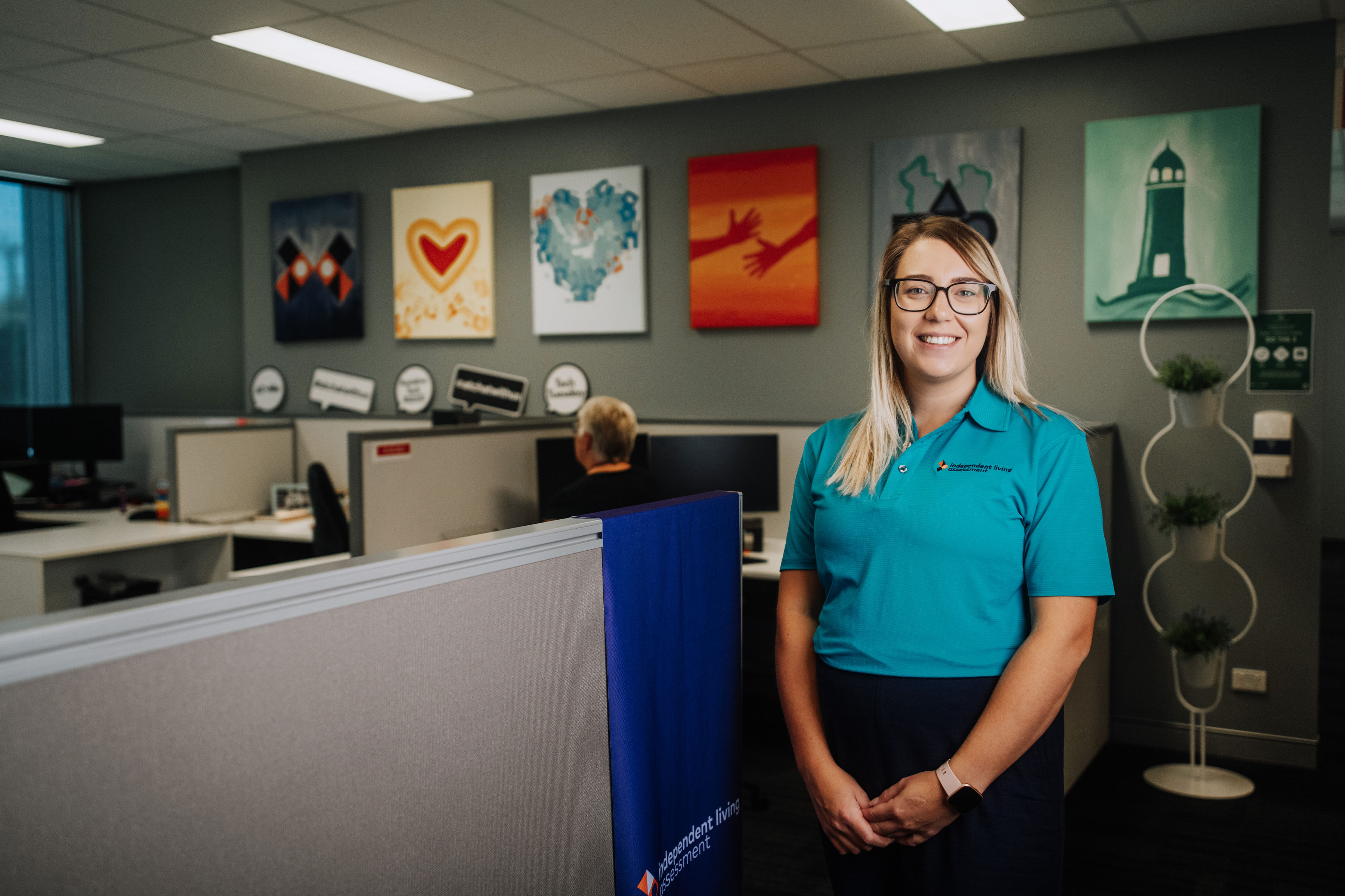 Female in ILA uniforms standing in office area with Values pictures in background Professional female with glasses smiling standing in office area with ILA value pictures in background