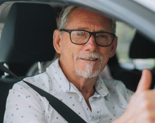 Indigo_OTDA_Customer Older male with a beard, wearing glasses giving a thumbs up from inside a car